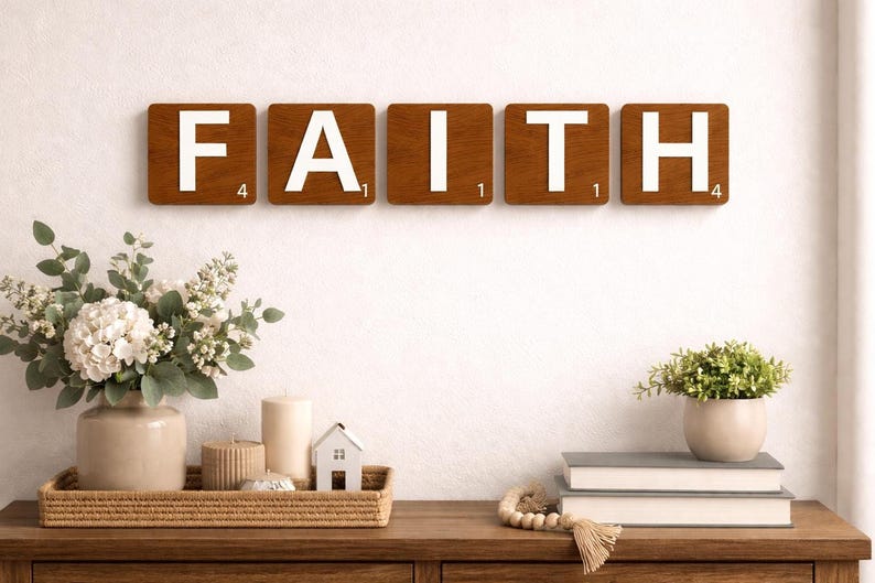 Six brown Scrabble tiles spell "FAITH" horizontally on a white wall above a wooden console table with decor.