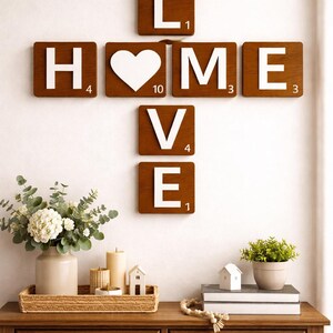 Brown Scrabble tiles spell "HOME" horizontally and "LOVE" vertically, intersecting at the "O", on a white wall above a wooden console table.