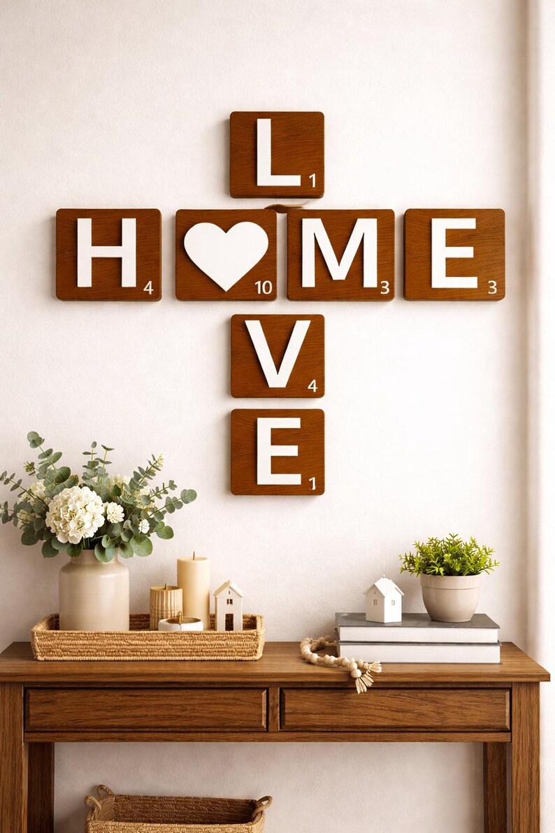 Brown Scrabble tiles spell "HOME" horizontally and "LOVE" vertically, intersecting at the "O", on a white wall above a wooden console table.