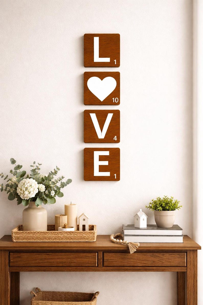 Four brown Scrabble tiles spell "LOVE" vertically on a white wall above a wooden console table with decor.