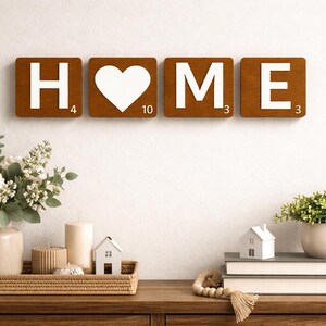 Four brown Scrabble tiles spell "HOME" on a white wall above a wooden console table with decor.