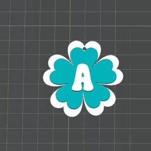 May include: A turquoise and white flower-shaped ornament with the letter "A" in the center. The ornament has a four-petal design with a white outline and a small hole at the top for hanging. The background is a dark gray grid.