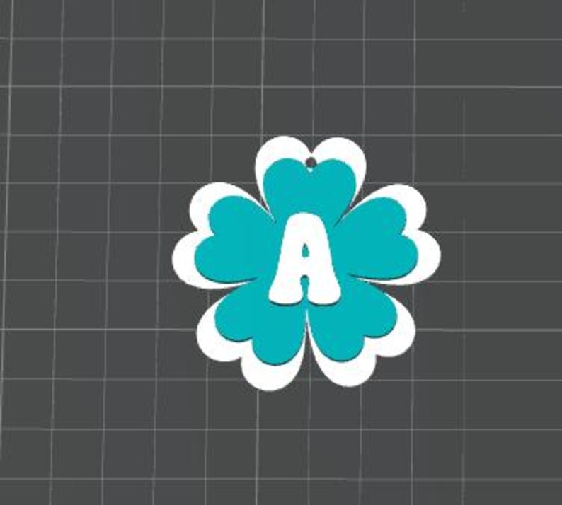 May include: A turquoise and white flower-shaped ornament with the letter "A" in the center. The ornament has a four-petal design with a white outline and a small hole at the top for hanging. The background is a dark gray grid.