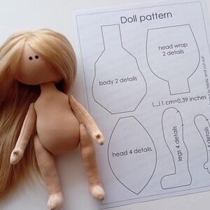 May include: A handmade doll with long blonde hair and a fabric body, next to a printed doll pattern. The pattern includes outlines for the body, head, legs, and arms, with text indicating the number of details needed. The pattern includes a measurement of 1 cm = 0.39 inches.