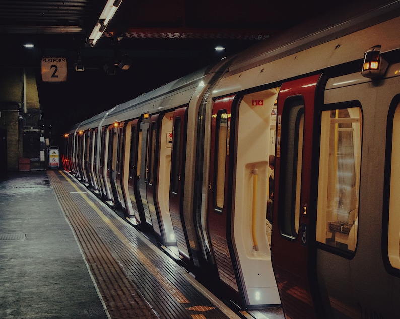 May include: A London Underground train at a station platform. The train has red and silver carriages, with some doors open. The platform is marked with yellow lines and the sign "Platform 2". The scene is dark.