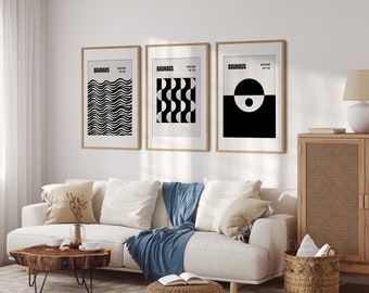 May include: Three framed Bauhaus art prints with geometric designs in black and white. The prints are displayed above a white sofa with blue and beige throw pillows. The frames are a light wood color, and the overall aesthetic is modern and minimalist.