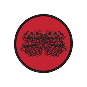Könnte beinhalten: Ein runder, roter Aufnäher mit einem schwarzen, gestickten Rand. Der Aufnäher zeigt ein schwarzes, stilisiertes Design mit dem Text "RETA MINOS" in einer gotischen Schriftart. Das Design ist mittig auf dem Aufnäher platziert.