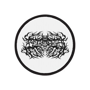 Puede incluir: Un parche redondo blanco con borde negro. El parche presenta un diseño negro estilizado de estilo tribal con la palabra "RETAMINOPH" en el centro. El diseño es simétrico e intrincado.