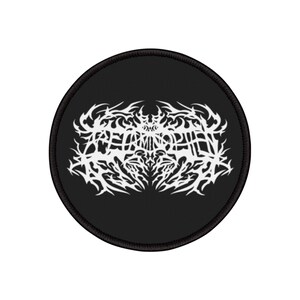Könnte beinhalten: Ein runder, schwarzer Aufnäher mit einem weißen, kunstvollen Design, möglicherweise ein Bandlogo oder -emblem. Das weiße Design ist kompliziert und stilisiert, mit einem schwarzen Rand. Der Aufnäher ist wahrscheinlich aus Stoff und für Kleidung geeignet.