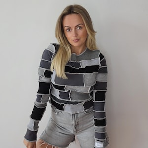 Peut inclure: Un haut à manches longues en patchwork dans les tons de gris et de noir. Le haut présente une texture côtelée et un design unique, associé à un short en jean gris. Les manches ont un détail de poignet avec une petite étiquette.