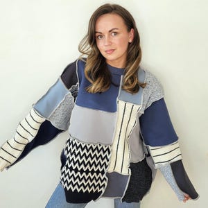 Può includere: Un maglione patchwork nei toni del blu, grigio e nero. Il maglione presenta un mix di trame e motivi, tra cui tessuti a maglia e tessuti. Le maniche hanno dettagli a righe e a zig-zag, e il design generale è unico e accattivante.
