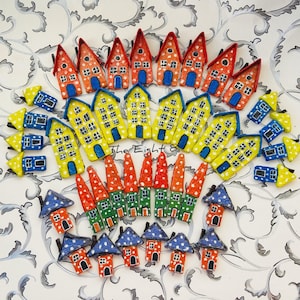 Könnte beinhalten: Eine Sammlung farbenfroher Miniaturhäuser, kreisförmig angeordnet. Die Häuser weisen verschiedene Designs auf, darunter Rot, Orange, Gelb, Grün und Blau, mit Tupfen und Fensterdetails. The Eight ist auf dem Bild geschrieben.