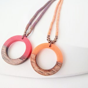 Puede incluir: Dos collares con colgantes circulares de madera y resina. Un colgante es rojo y naranja, el otro es naranja y marrón. Los collares están hechos con pequeñas cuentas.