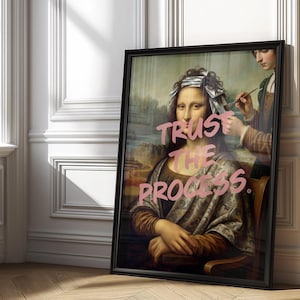 May include: A framed art print showing a parody of the Mona Lisa with the words "Trust the Process" in pink. The image depicts the Mona Lisa having her hair styled. The frame is black.