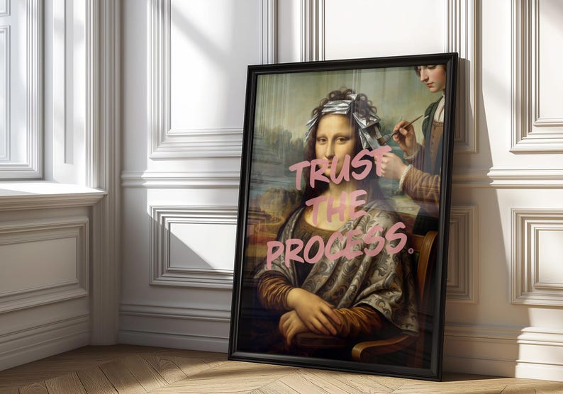 May include: A framed art print showing a parody of the Mona Lisa with the words "Trust the Process" in pink. The image depicts the Mona Lisa having her hair styled. The frame is black.