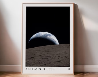 May include: A framed print depicting Earth rising over the Moon's surface, with the text "ARTEMIS II" at the bottom. The image shows a blue and white Earth against a black sky, with a textured grey lunar surface in the foreground.