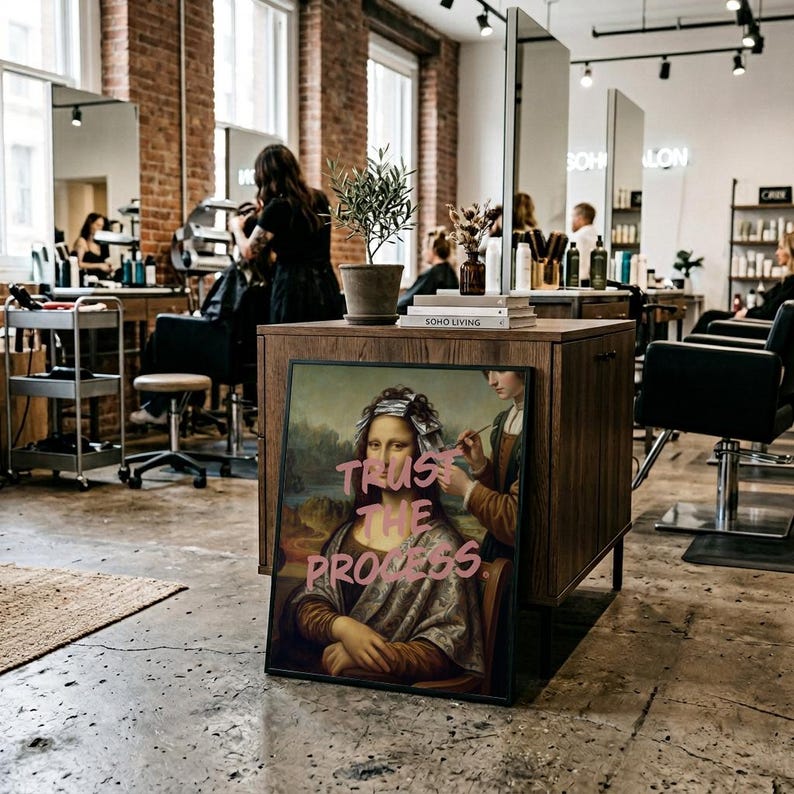 May include: A framed print of the Mona Lisa with the words "TRUST THE PROCESS" in pink graffiti-style lettering. The image is set in a hair salon with stylists working on clients, mirrors, and a wooden cabinet.