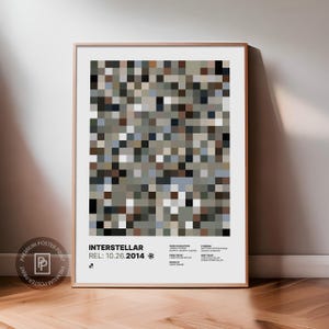 Può includere: Un poster incorniciato con il titolo "INTERSTELLAR" e la data di uscita "10.26.2014". L'opera presenta un mosaico di piccoli quadrati nei toni del grigio, marrone e blu. Il poster è in una cornice di legno ed è esposto su un muro.