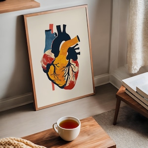 May include: Anatomy-themed art print featuring a stylized human heart illustration. The artwork uses a palette of red, yellow, blue, and black against a cream background. The print is framed in a thin, copper-colored frame and leans against a wall.