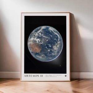 May include: A framed print featuring a detailed image of Earth from space, showcasing continents, oceans, and cloud formations against a black background. The print includes the text "ARTEMIS II" at the bottom.