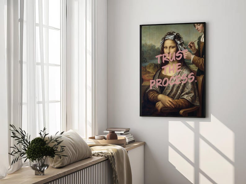 May include: A framed art print of the Mona Lisa with the text "Trust the Process" in pink. The artwork is displayed on a white wall near a window with sheer curtains. The print has a black frame.
