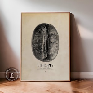 Op de afbeelding: Een ingelijste poster met een gedetailleerde, grijswaardenafbeelding van een koffieboon. Het oppervlak van de boon is getextureerd, met een kaartachtig patroon. Het woord "ETHIOPIA" staat onder de boon, samen met "Yirgacheffe, Sidamo". De poster zit in een houten lijst.