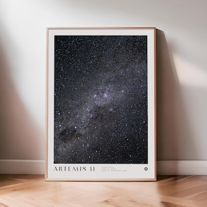 Puede incluir: Una impresión enmarcada que presenta una imagen detallada de un cielo nocturno estrellado. La imagen está dominada por azules oscuros y negros, con grupos de estrellas brillantes y un efecto de vía láctea. La impresión está etiquetada "ARTEMIS II".