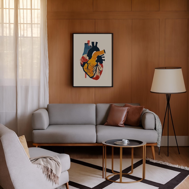 May include: A framed anatomical heart print in a living room setting. The artwork features a colorful illustration of a human heart with red, yellow, blue, and black hues. The room includes a gray sofa, a side table, and a floor lamp.