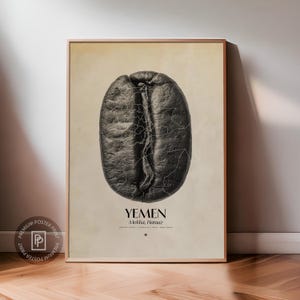 Può includere: Un poster incorniciato con un'immagine in scala di grigi di un chicco di caffè. La superficie del chicco è strutturata, con un design simile a una mappa sovrapposta. Il testo "YEMEN Molkha, Haraaz" è sotto il chicco.