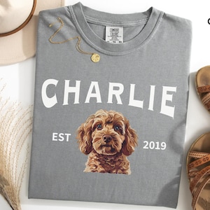 May include: Grey t-shirt with a white graphic of a dog with the text "Charlie Est 2019".