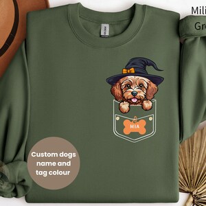 Peut inclure: Un sweat-shirt vert avec une poche représentant un chien de dessin animé portant un chapeau de sorcière. Le nom du chien, "MIA", est sur une étiquette en forme d'os dans la poche. Le sweat-shirt est disponible en couleurs personnalisées et avec un nom de chien personnalisé.