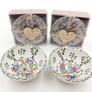 Puede incluir: Cuencos de cerámica pintados a mano con diseños florales y de pájaros en tonos azules, rojos, amarillos y verdes. Los cuencos tienen un borde festoneado y están empaquetados en cajas transparentes con etiquetas de corazón de madera que dicen "Wesley Thank you Elizabeth."