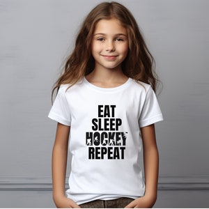 May include: White t-shirt with black text that reads "Eat Sleep Hockey Repeat" with hockey player silhouettes incorporated into the text.