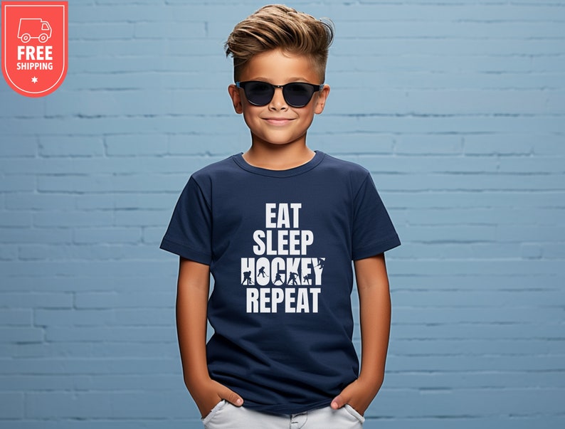 May include: A navy blue t-shirt with white text that reads "Eat Sleep Hockey Repeat". The shirt features a graphic of hockey players.