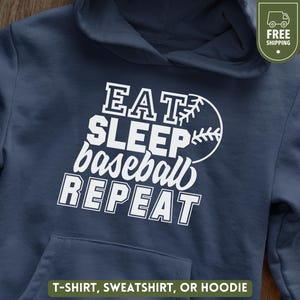 Könnte beinhalten: Marineblauer Hoodie mit Fronttasche und Kapuze. Der weiße Text lautet "EAT SLEEP baseball REPEAT" mit einer Baseball-Grafik. Der untere Teil des Bildes lautet "T-SHIRT, SWEATSHIRT, ODER HOODIE".