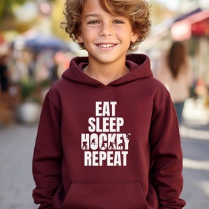 May include: Burgundy hooded sweatshirt with the text "Eat Sleep Hockey Repeat" in white. The text is surrounded by hockey player silhouettes.