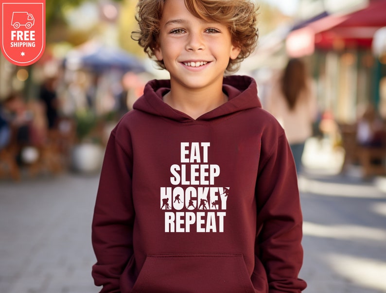 May include: Burgundy hooded sweatshirt with the text "Eat Sleep Hockey Repeat" in white. The text is surrounded by hockey player silhouettes.