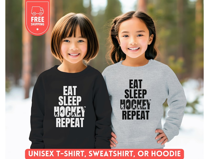 May include: Two children wearing sweatshirts with the text "Eat Sleep Hockey Repeat" printed on them. The sweatshirts are black and gray. The children are smiling.