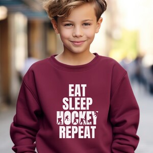 May include: A maroon sweatshirt with white text that reads "Eat Sleep Hockey Repeat" and a graphic of hockey players.