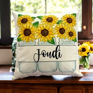 15 x 15 pillow with white background with a printed image of three mason jars filled with yellow sunflowers with a custom family name in a cutout in the mason jars in a script font and black ink