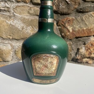 May include: A green glass bottle with a silver top and a label that reads "By an ancient custom originating in the Royal Navy a salute of twenty-one guns is the prerogative of the Reigning Sovereign. Royal Salute Whisky, created to celebrate the Coronation of Her Majesty Queen Elizabeth symbolizes this homage."