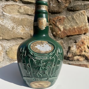 May include: A green ceramic bottle of Chivas Regal Scotch Whisky with a gold label and a silver top. The bottle features a crest with a knight on horseback and the text "CHIVAS" and "ESTD 1801".