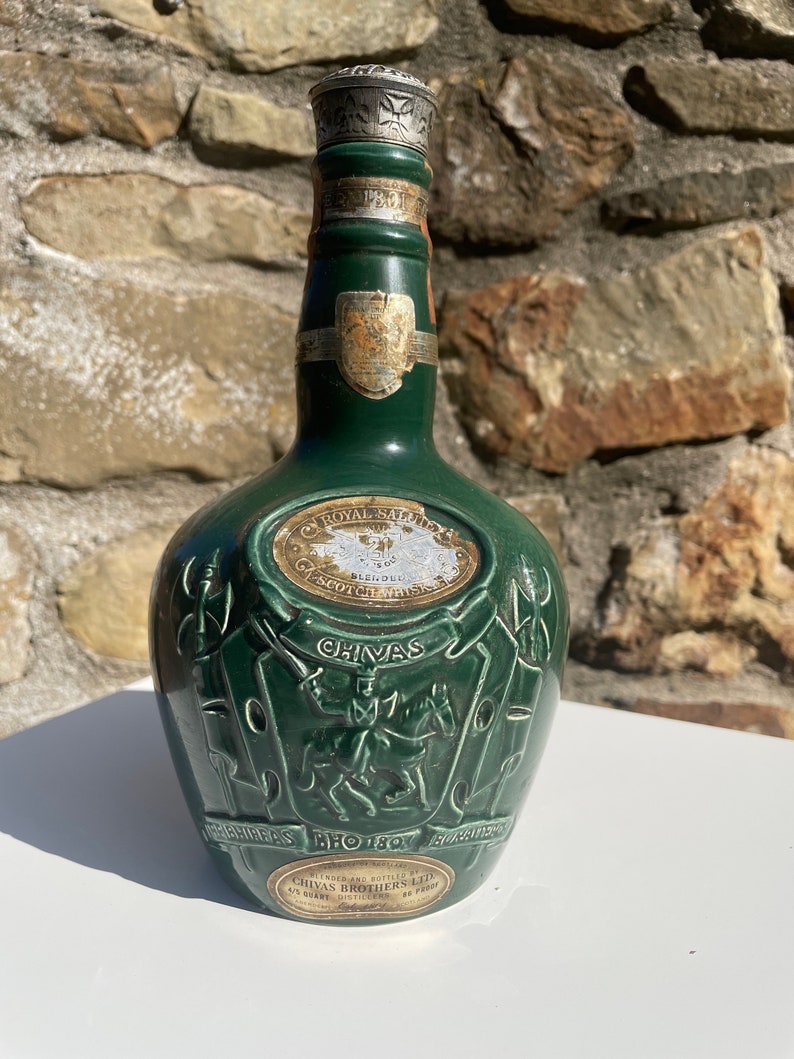 May include: A green ceramic bottle of Chivas Regal Scotch Whisky with a gold label and a silver top. The bottle features a crest with a knight on horseback and the text "CHIVAS" and "ESTD 1801".