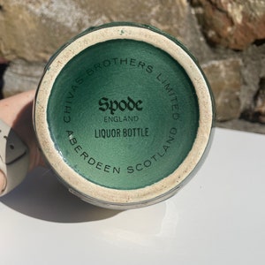 May include: Close-up of the bottom of a green ceramic liquor bottle with the text "Chivas Brothers Limited Aberdeen Scotland" and "Spode England Liquor Bottle" printed on it.
