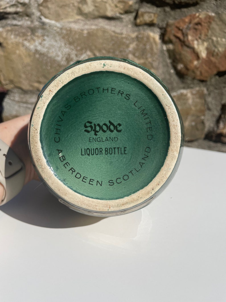 May include: Close-up of the bottom of a green ceramic liquor bottle with the text "Chivas Brothers Limited Aberdeen Scotland" and "Spode England Liquor Bottle" printed on it.