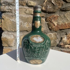 May include: A green glass bottle of Chivas Regal Scotch Whisky with a silver top. The bottle has a label with the words "Chivas Regal" and "Scotch Whisky" on it. The bottle is sitting on a white surface.