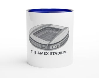 May include: White ceramic mug with a blue interior featuring a detailed illustration of The Amex Stadium. The stadium image is in grayscale, with the text "THE AMEX STADIUM" printed below the image in black.