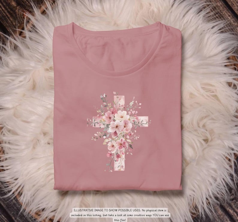 以下が含まれることがあります： ピンクがかったバラ色のTシャツ。花の十字架のデザインが特徴です。十字架はピンクと白の花と緑の葉で飾られています。シャツは折りたたまれ、ふわふわの白い表面に置かれています。下部のテキストは次のとおりです：ILLUSTRATIVE IMAGE TO SHOW POSSIBLE USES.