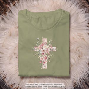 以下が含まれることがあります： セージグリーンのTシャツ。花の十字架のデザインが特徴です。十字架はピンクと白の花と緑の葉で飾られています。Tシャツはふわふわの白い表面に折りたたまれています。下部のテキストは次のとおりです: ILLUSTRATIVE IMAGE TO SHOW POSSIBLE USES.