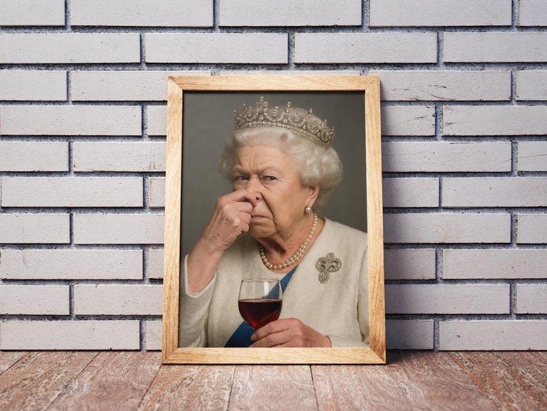 May include: A framed portrait of Queen Elizabeth II, wearing a crown and pearl necklace, holding a glass of red wine. The Queen is pinching her nose. The frame is made of light brown wood, and the background is a brick wall.